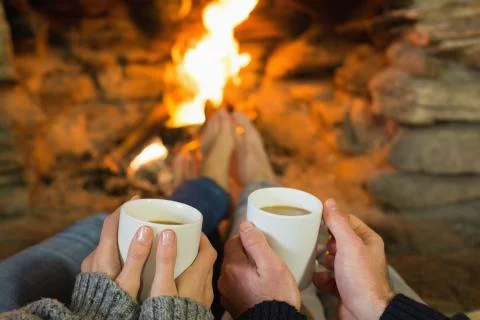 Hands holding coffee cups in front of lit fireplace Stock Photos