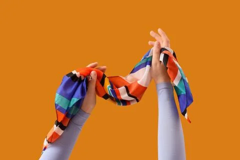 Hands holding colorful patterned scarf against orange background, fashion acc Stock Photos
