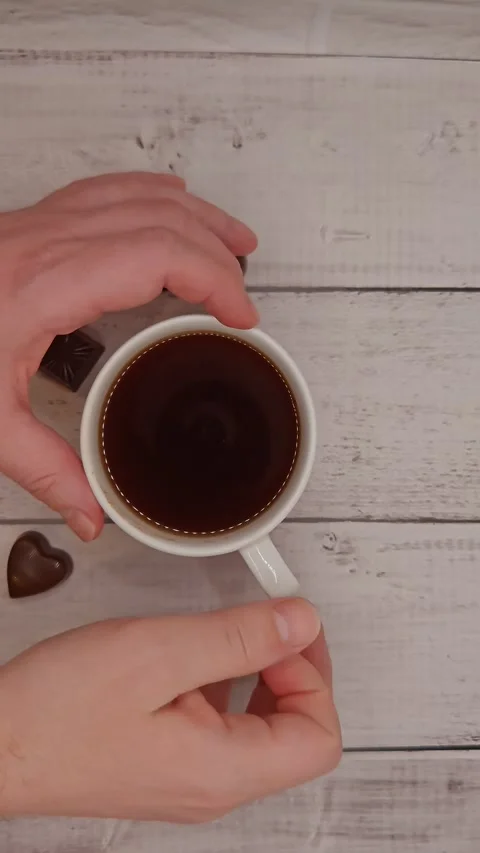 Hands holding a cup of coffee and sweet candies on the table Stock Footage 329939109