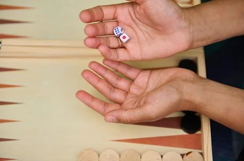 Hands holding dice over a backgammon board ready to play a game Stock Photos