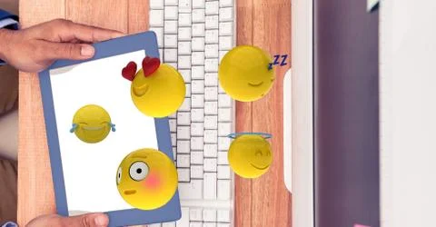 Hands holding digital tablet while emojis flying over computer desk Stock-Fotos