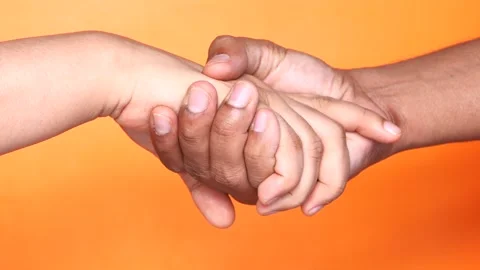 Hands holding each other tightly against orange background showing concept .. Stock Footage 332578625