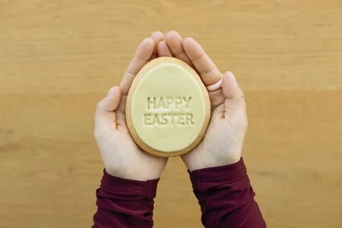 Hands holding Easter cookie with Happy Easter text on wooden background. Stock Photos