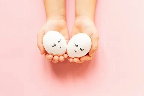 Hands holding easter eggs with cute face and sleepy eyes on pastel pink backg Stock Photos