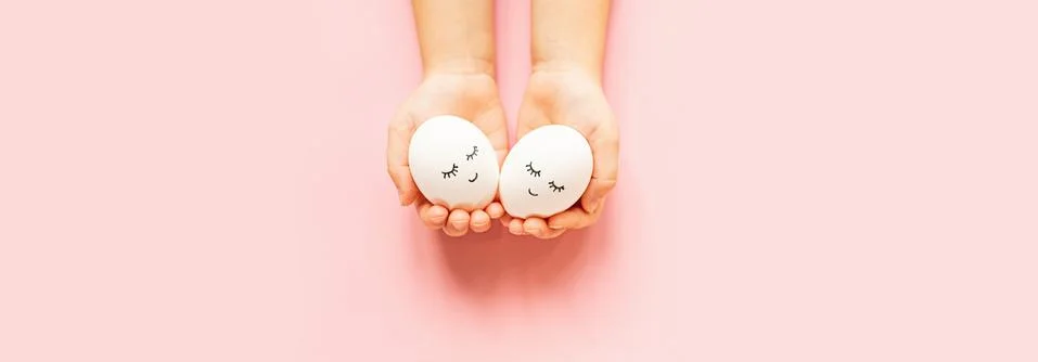 Hands holding easter eggs with cute face and sleepy eyes on pastel pink backg Stock-Fotos