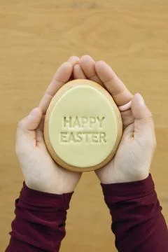 Hands holding egg shaped Easter cookie with Happy Easter text. Stock Photos