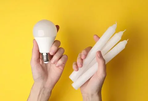 Hands holding energy-saving light bulb and white candles Stock Photos