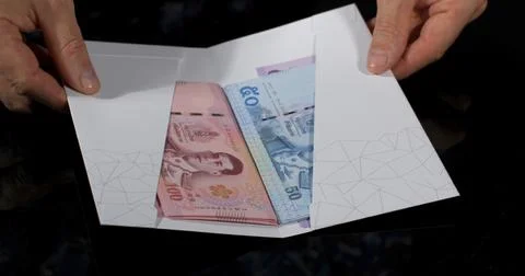 Hands holding an envelope that contains different banknotes in a simple setting Stock Photos