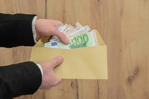 Hands holding an envelope with a stack of euro banknotes in a business settin Stock Photos