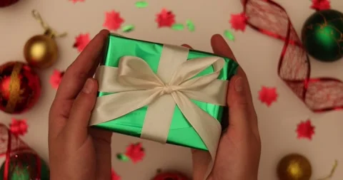 Hands holding a festive green gift box with a white ribbon, surrounded by Stock Footage 339071184