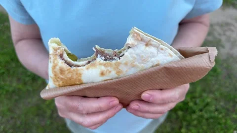 Hands holding a flatbread with grilled meat wrapped in brown paper outdoors Stock Footage 337774874