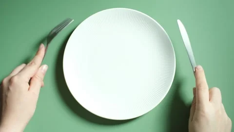 Hands holding a fork and knife next to an empty plate on a green background. Stock Footage 285496164