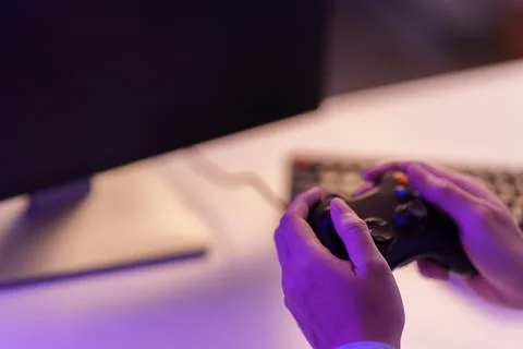 Hands holding game controller at computer desk for video gaming Stock Photos