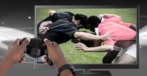 Hands holding gaming controller  with rugby players on television Stock Photos