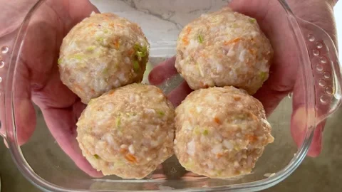 Hands holding a glass baking dish with four raw meatballs mixed with rice Stock Footage 345327324