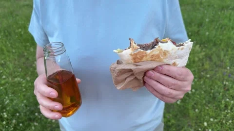 Hands holding a grilled meat wrap and a glass bottle of apple juice 動画素材 337774713