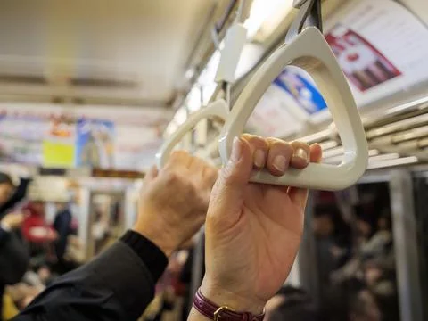 Hands holding on to handles to support themselves while standing on a busy Stock-Fotos