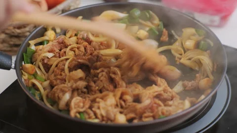 Hands holding a ladle stir-frying kimchi and kurobuta pork in a wok in kitchen. Stock Footage 242552193