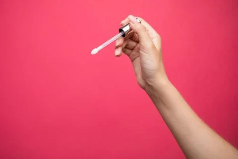 Hands holding lip gloss applicator on pink background. Stock Photos
