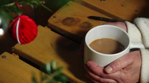Hands holding mug of steaming hot coffee with Christmas gifts and wrapping 库存影片 328865771