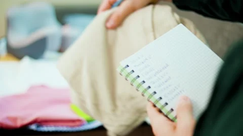Hands holding a notebook, checking off a packing list with a pen. Preparing lugg Stock Footage 340653922