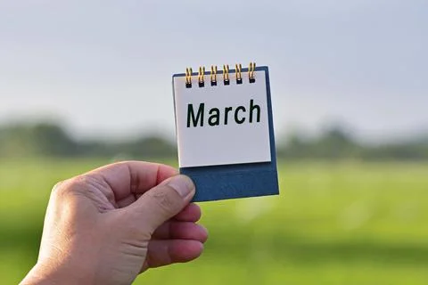 Hands Holding A Notepad With March Text Written And Blurred Green Background Stock Photos