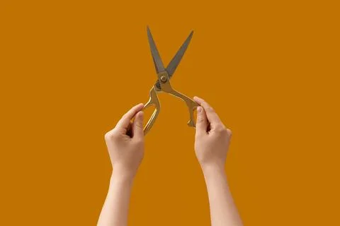 Hands holding open gold scissors against a solid orange background, crafting  Stock Photos