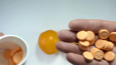 Hands holding orange-patterned vitamins next to orange fruit in 4K Video stock 142958746