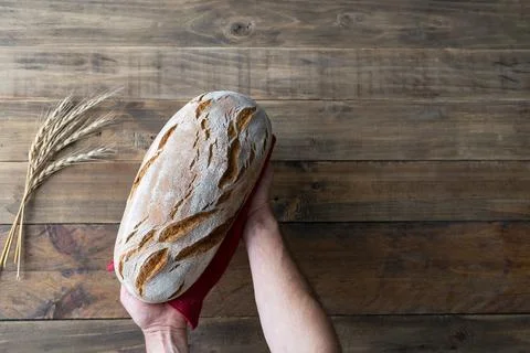 Hands holding a piece of rustic bread on wooden background with red napkin .. Stock Photos