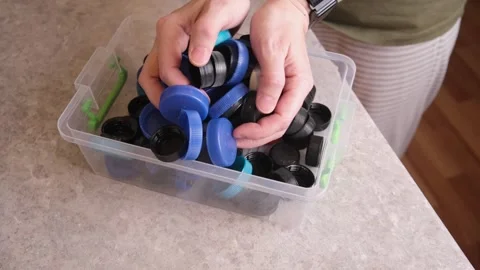 Hands holding pile of colorful plastic bottle caps over clear box Stock Footage 322056441