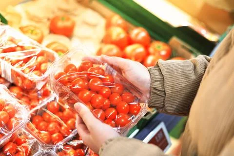 Hands holding a plastic container of bright red cherry tomatoes in the prod.. Stock Photos