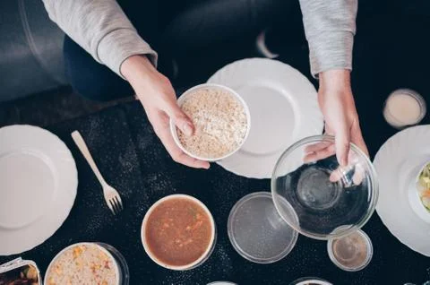 Hands holding a plastic container with rice and an empty glass bowl Stock Photos