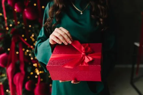 Hands holding red present in front of decorated Christmas tree. Stock Photos