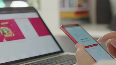 Hands Holding Red Smartphone Displaying Shopping App Near Laptop 動画素材 336527661