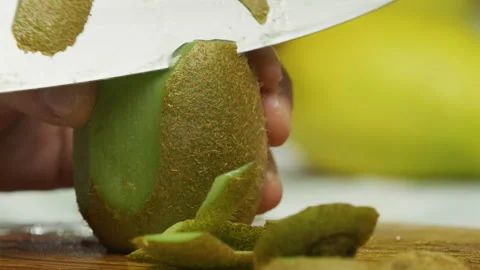 Hands holding sharp knife and carefully cutting skin off kiwi - closeup, slow Stock Footage 341271736