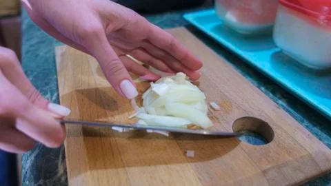 Hands holding sharp knife and chopping fresh white onion on kitchen. Stock Photos
