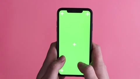 Hands holding a smartphone with a green screen and tracking markers on a pink Stock Footage 339189634