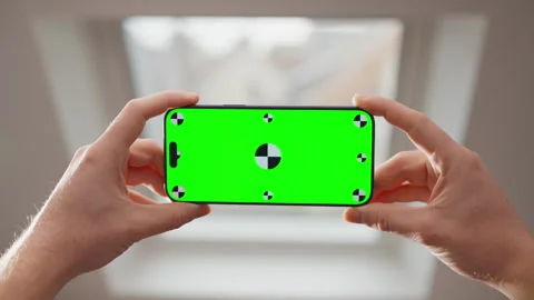 Hands Holding Smartphone with Green Screen Mockup in Bright Indoor Home Setting Stock Footage 345847161
