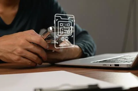 Hands Holding Smartphone with QR Code Overlay on Laptop Desk Stock Photos