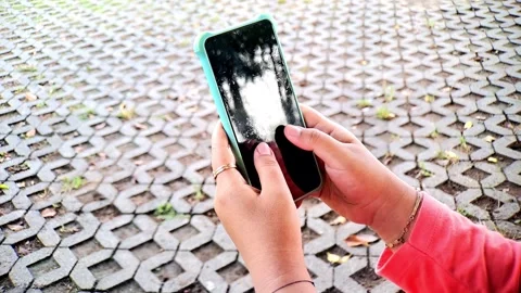 Hands Holding Smartphone with Teal Case on Textured Pavement Background Stock Footage 321116536