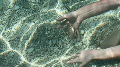 Hands Holding Smooth Pebbles Underneath the Crystal-Clear Surface of the Sea Stock Footage 318086565