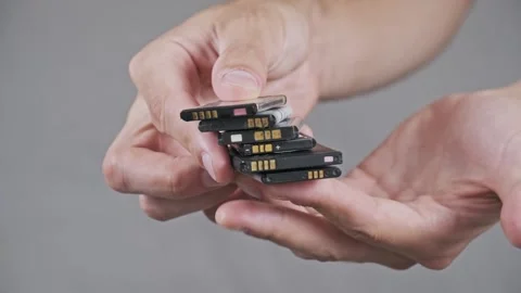 Hands Holding a Stack of Used Lithium-Ion Phone Batteries for Recycling Stock Footage 315410315