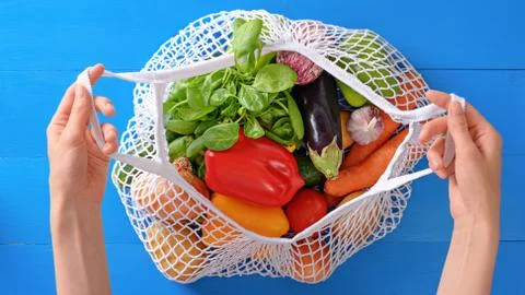 Hands holding string bag with vegetables on blue background, eco shopping, to Stock Photos