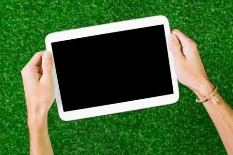 Hands holding a tablet with a blank screen against an artificial grass Stock Photos