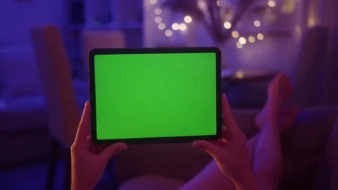Hands holding a tablet with green screen display. Female relaxing on a sofa at Stock Footage 282374021