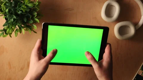 Hands holding a tablet with a green screen on a wooden desk with headphones Stockbeeldmateriaal 341737503