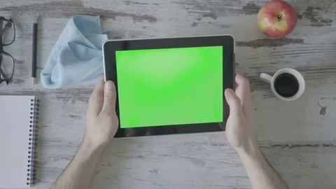 Hands holding tablet pc with green empty screen on wooden background Video stock 80246886