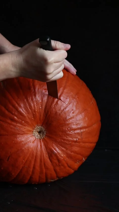 Hands holding the tail of a large pumpkin and carefully cutting it Video stock 347586049