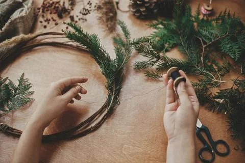 Hands holding thread and cedar branches , pine cones, scissors on wooden tabl Stock Photos