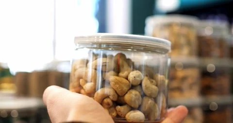 Hands holding a transparent plastic jar filled with cashew nuts, inside a Vidéo 309046838